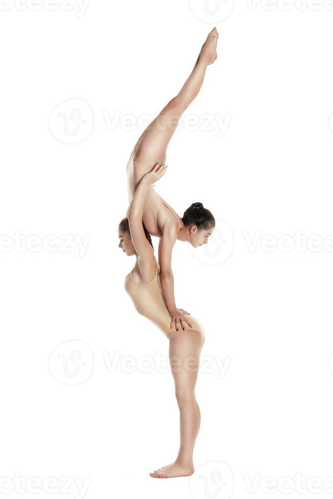 dos flexible muchachas gimnastas en beige leotardos son ejecutando ejercicios utilizando apoyo y posando aislado en blanco antecedentes. de cerca. foto