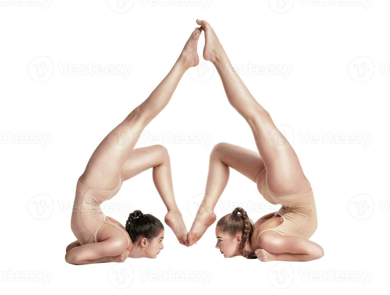 dos flexible muchachas gimnastas en beige leotardos ejecutando complejo elementos de gimnasia utilizando apoyo, posando aislado en blanco antecedentes. de cerca. foto