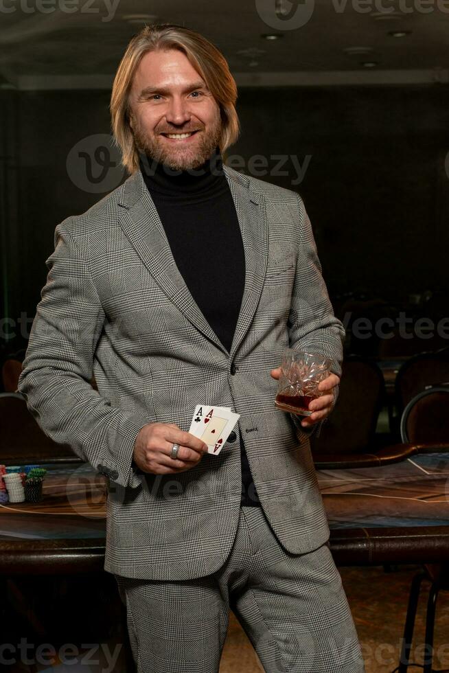 Lucky man standing near gaming table with glass of drink and set of winning pair of aces photo