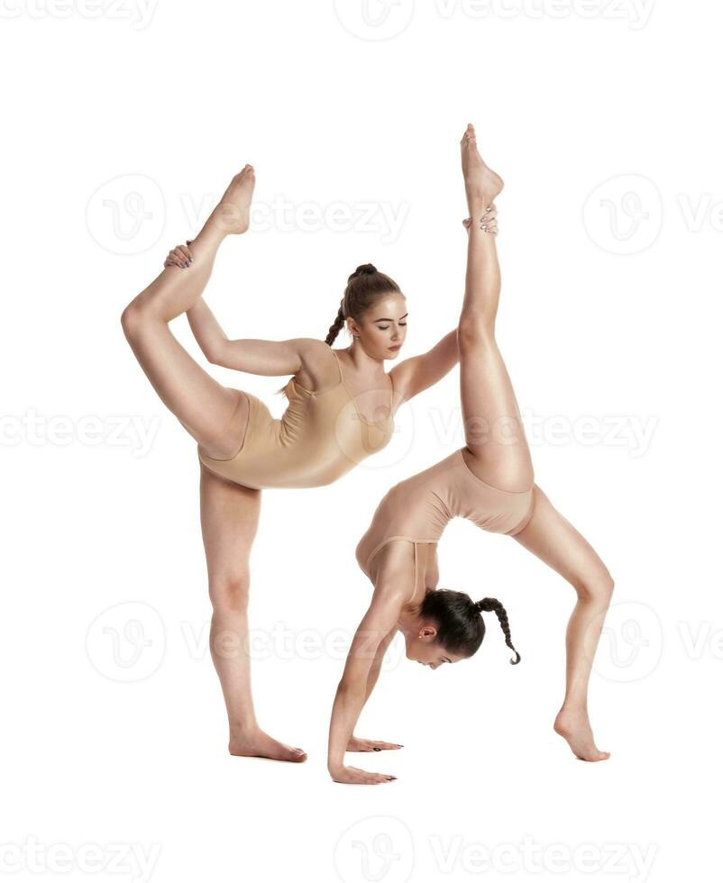 dos flexible muchachas gimnastas en beige leotardos ejecutando complejo elementos de gimnasia utilizando apoyo, posando aislado en blanco antecedentes. de cerca. foto