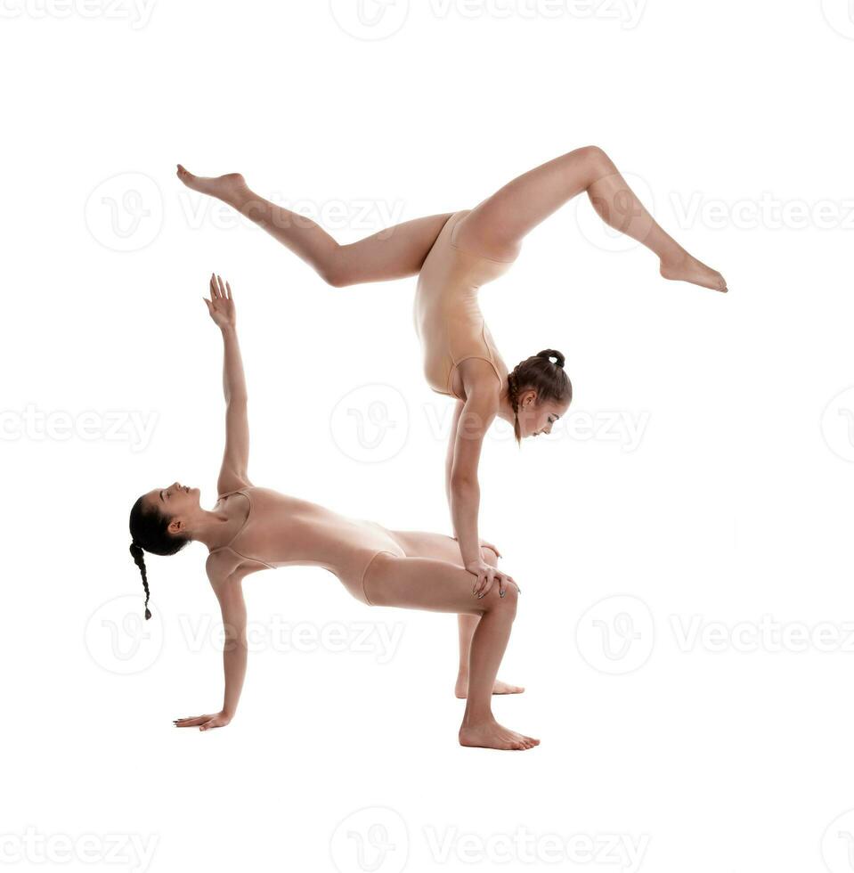 dos flexible muchachas gimnastas en beige leotardos son ejecutando ejercicios al revés abajo utilizando apoyo y posando aislado en blanco antecedentes. de cerca. foto