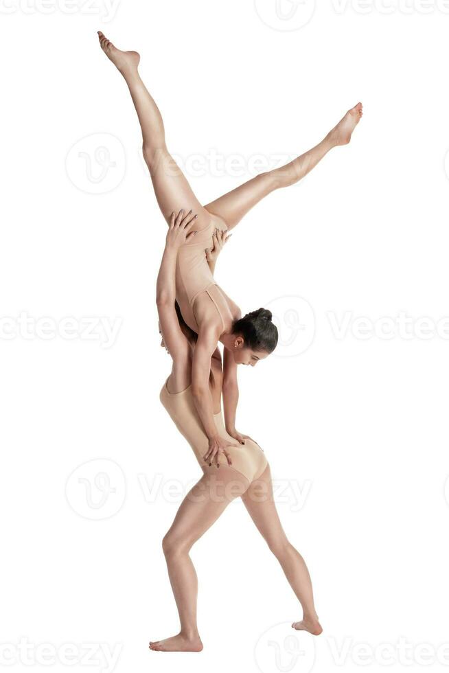 dos flexible muchachas gimnastas en beige leotardos ejecutando complejo elementos de gimnasia utilizando apoyo, posando aislado en blanco antecedentes. de cerca. foto