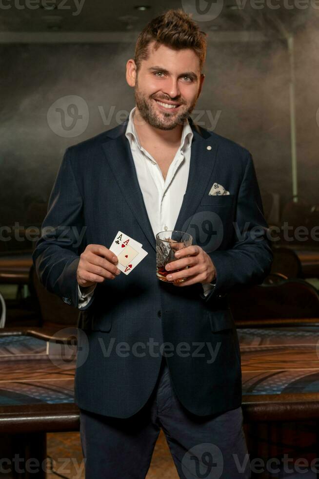exitoso póker jugador en pie cerca juego de azar mesa con par de ases y vaso de bebida foto