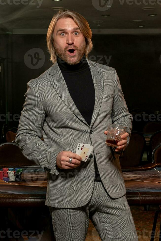 Surprised bearded man holding set of winning cards from pair of aces in casino photo