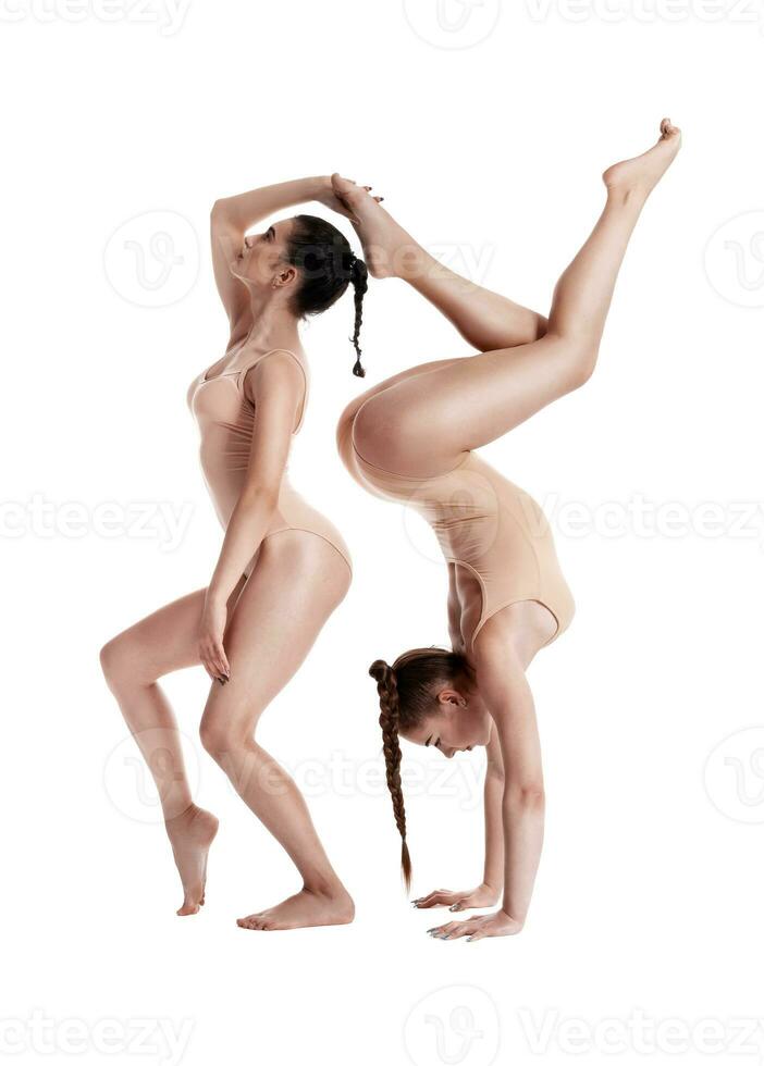 Two flexible girls gymnasts in beige leotards are performing exercises using support and posing isolated on white background. Close-up. photo