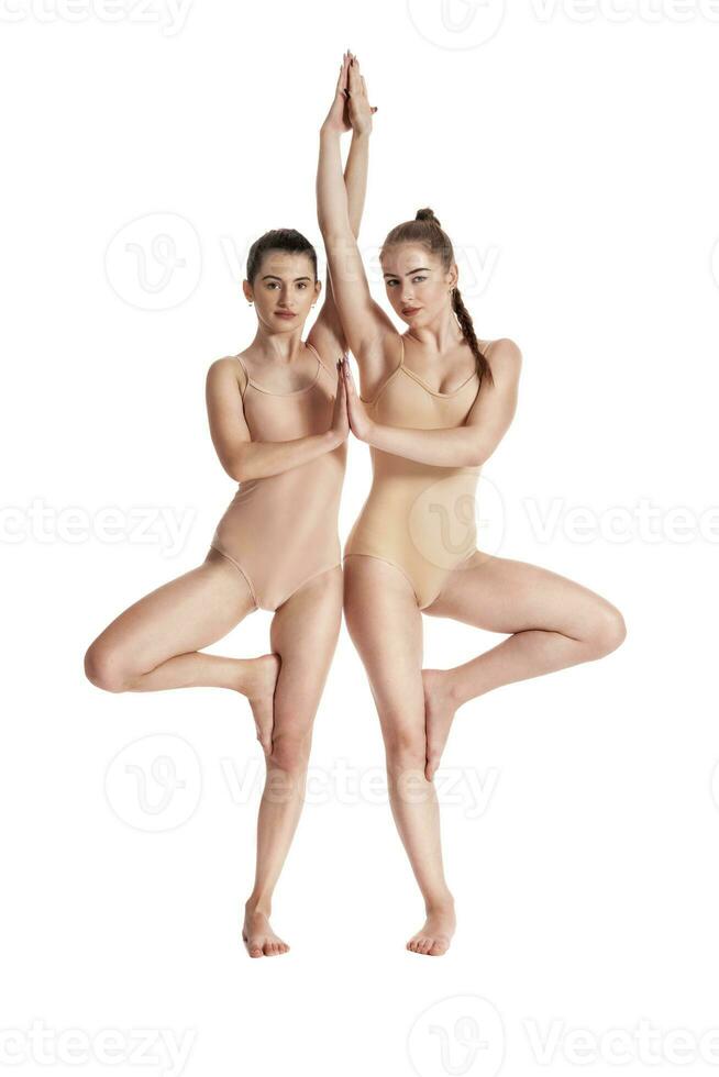 Two flexible girls gymnasts in beige leotards performing complex elements of gymnastics using support, posing isolated on white background. Close-up. photo