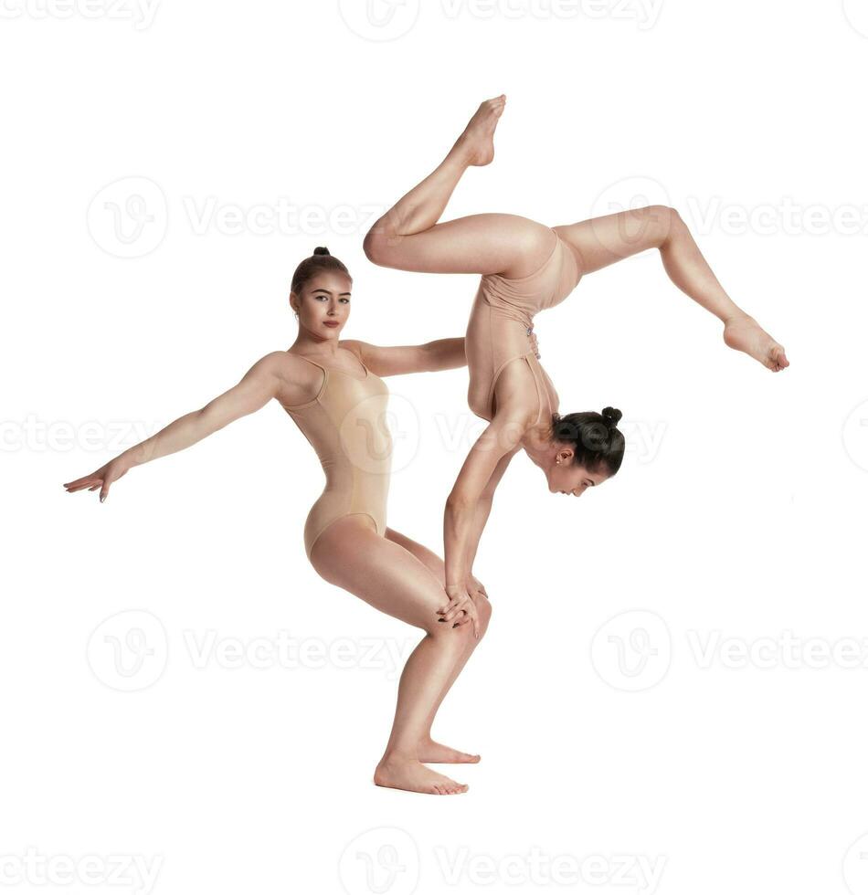 dos flexible muchachas gimnastas en beige leotardos son ejecutando ejercicios utilizando apoyo y posando aislado en blanco antecedentes. de cerca. foto