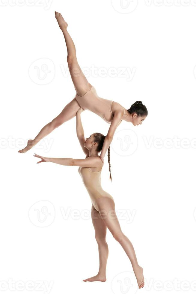 dos flexible muchachas gimnastas en beige leotardos ejecutando complejo elementos de gimnasia utilizando apoyo, posando aislado en blanco antecedentes. de cerca. foto