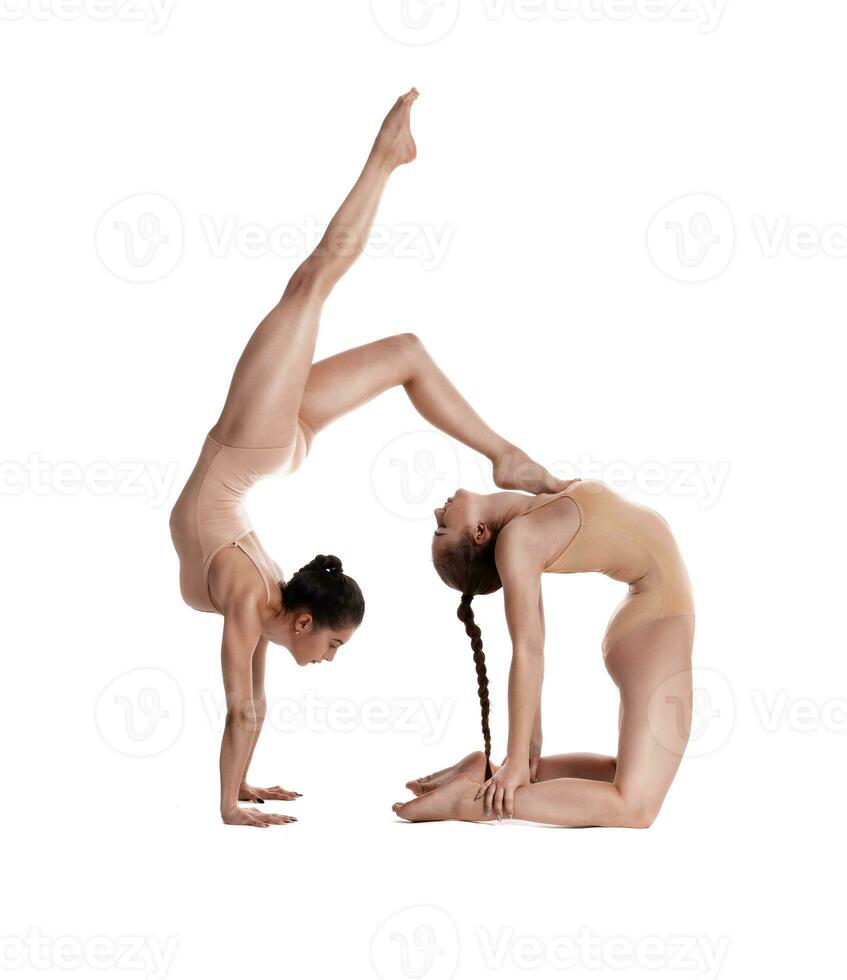 dos flexible muchachas gimnastas en beige leotardos son ejecutando ejercicios utilizando apoyo y posando aislado en blanco antecedentes. de cerca. foto