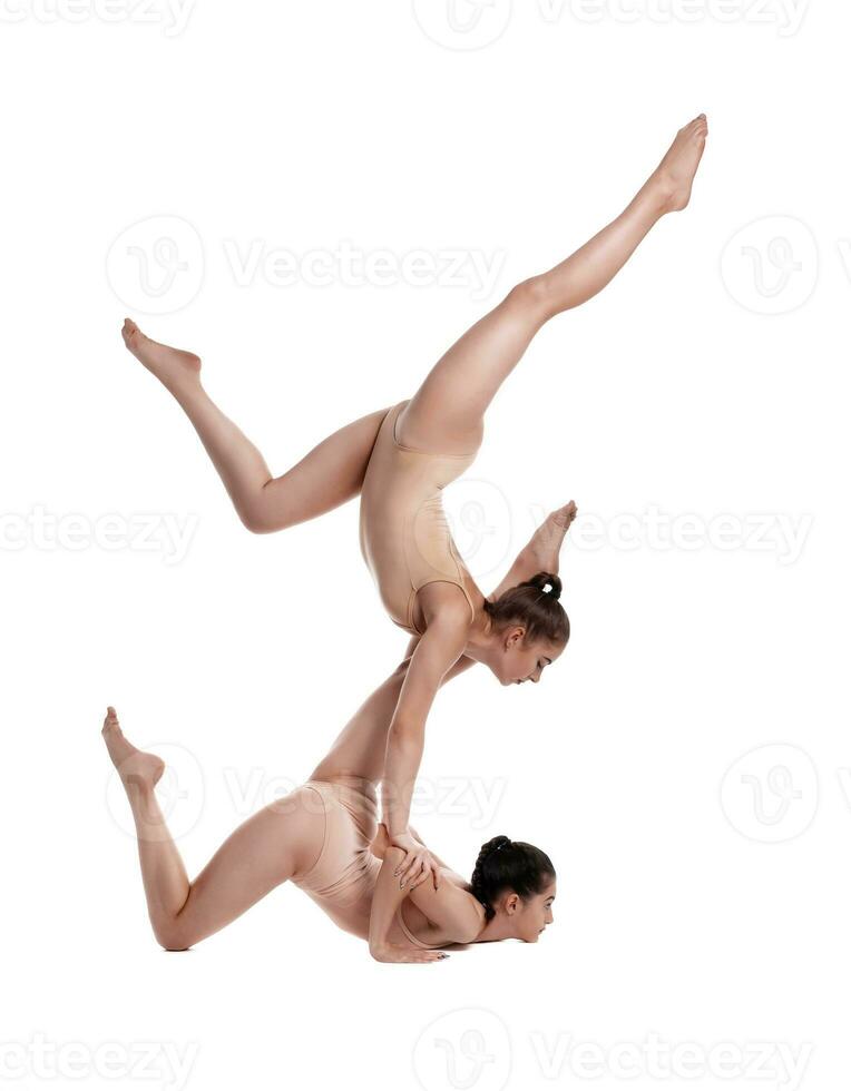 dos flexible muchachas gimnastas en beige leotardos son ejecutando ejercicios al revés abajo utilizando apoyo y posando aislado en blanco antecedentes. de cerca. foto