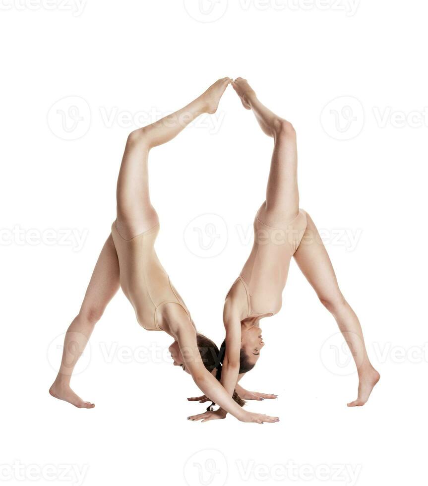 Two flexible girls gymnasts in beige leotards performing complex elements of gymnastics using support, posing isolated on white background. Close-up. photo