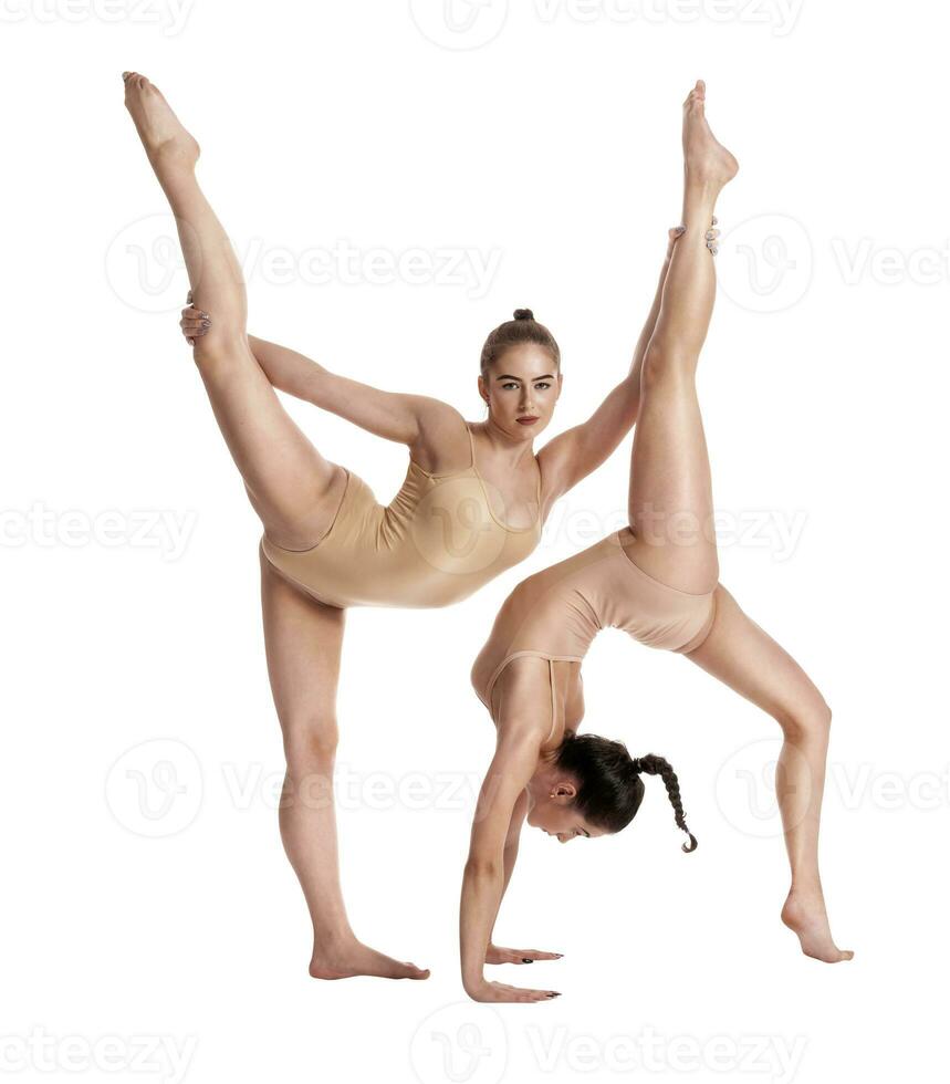 dos flexible muchachas gimnastas en beige leotardos ejecutando complejo elementos de gimnasia utilizando apoyo, posando aislado en blanco antecedentes. de cerca. foto