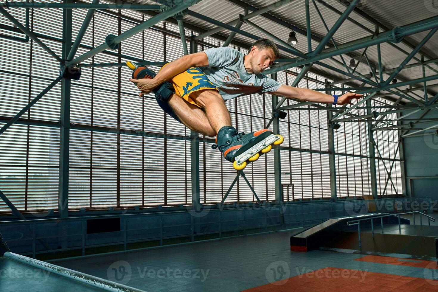 Rollerblader jump high from big air ramp performing trick. Indoors skate park equipment. photo