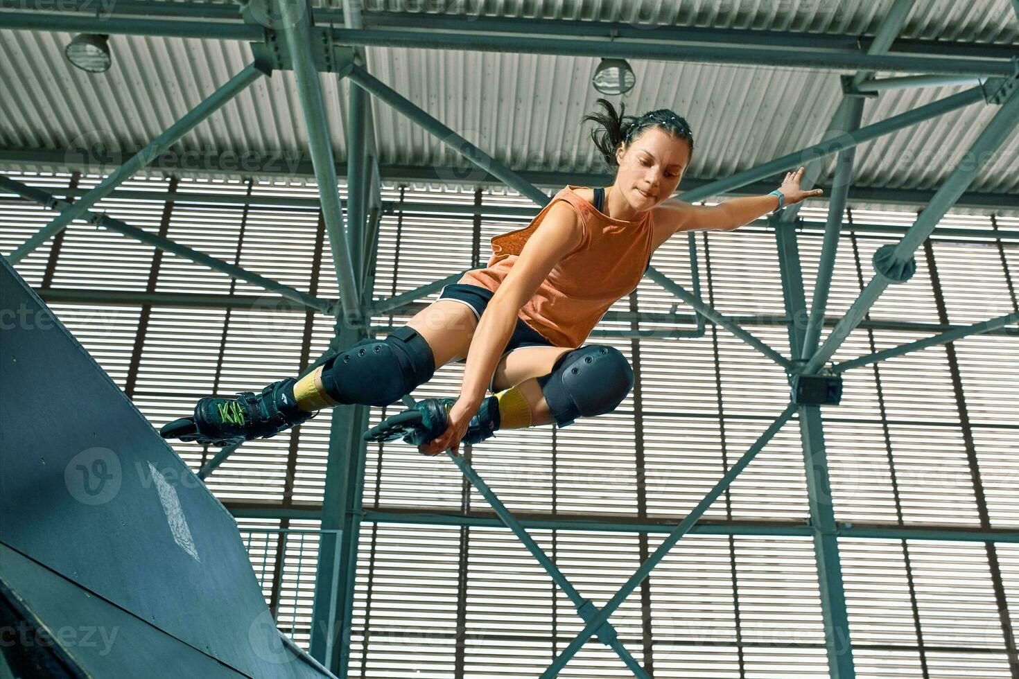 Rollerblader jump high from big air ramp performing trick. Indoors skate park equipment. photo
