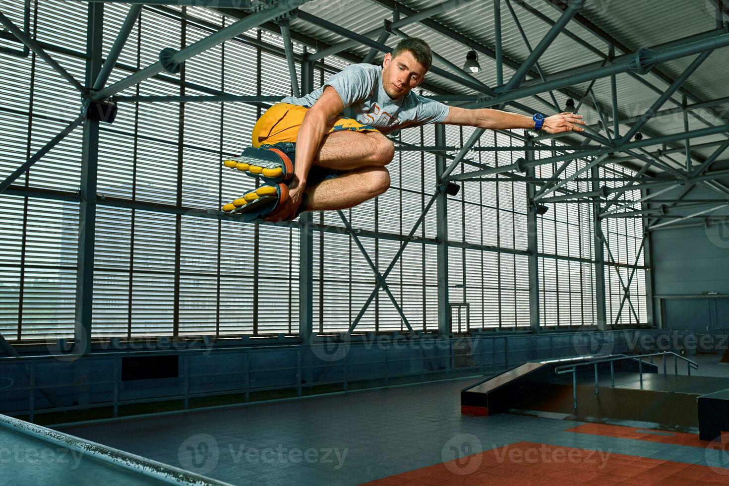 Rollerblader jump high from big air ramp performing trick. Indoors skate park equipment. photo