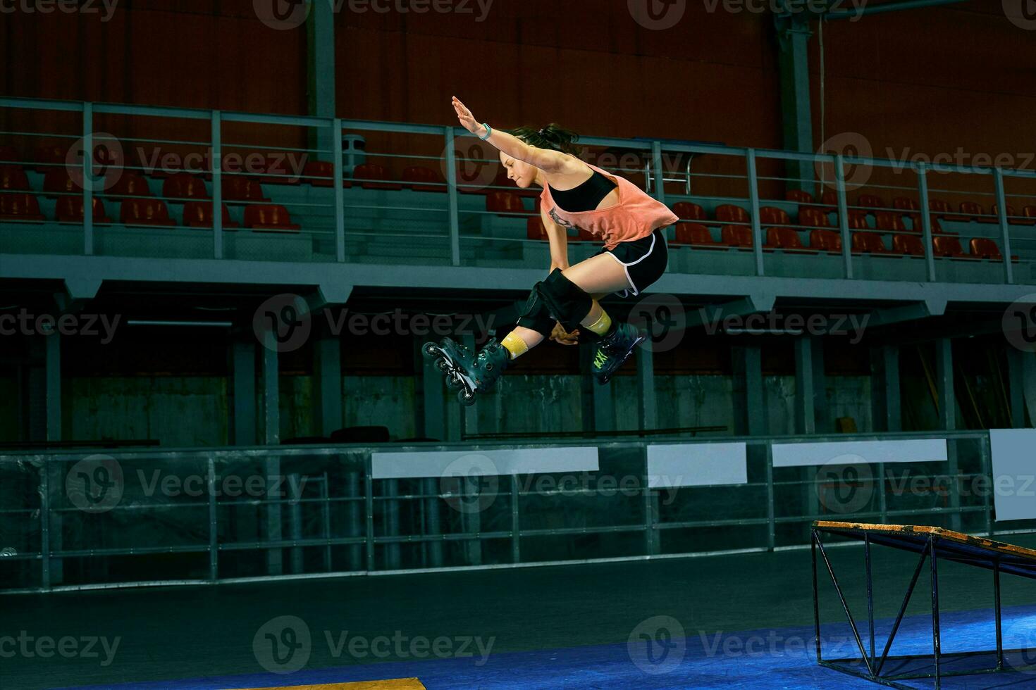 Rollerblader jump high from big air ramp performing trick. Indoors skate park equipment. photo