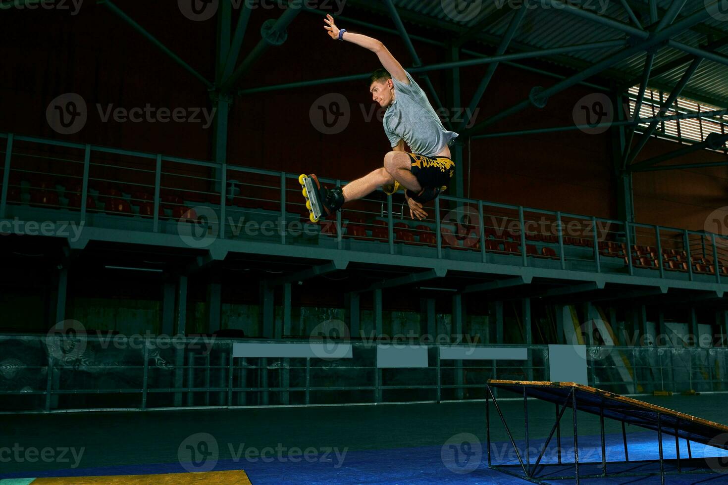 Rollerblader jump high from big air ramp performing trick. Indoors skate park equipment. photo