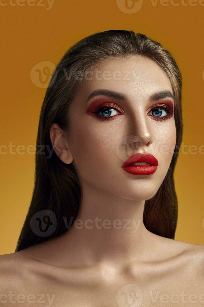 Close-up glamour portrait of a beautiful half-naked model with bright make-up posing over an orange background. photo