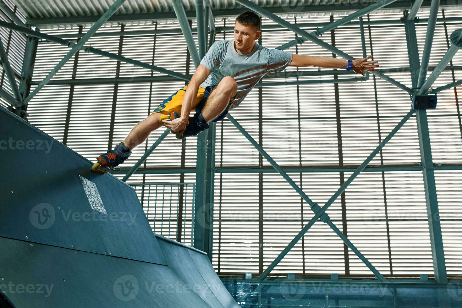 Rollerblader jump high from big air ramp performing trick. Indoors skate park equipment. photo