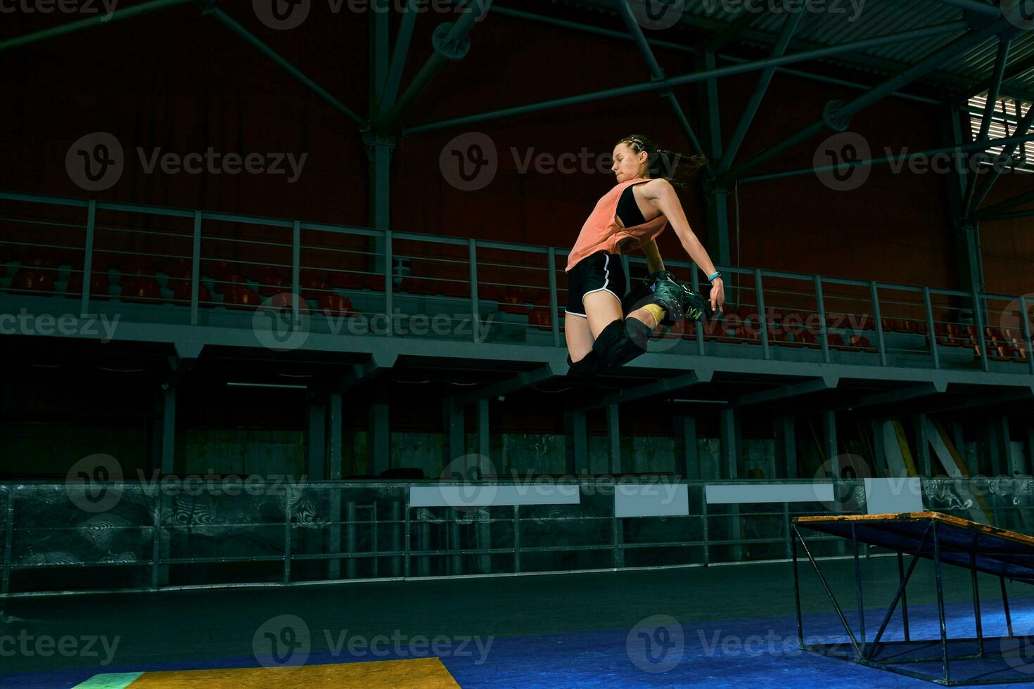Rollerblader jump high from big air ramp performing trick. Indoors skate park equipment. photo
