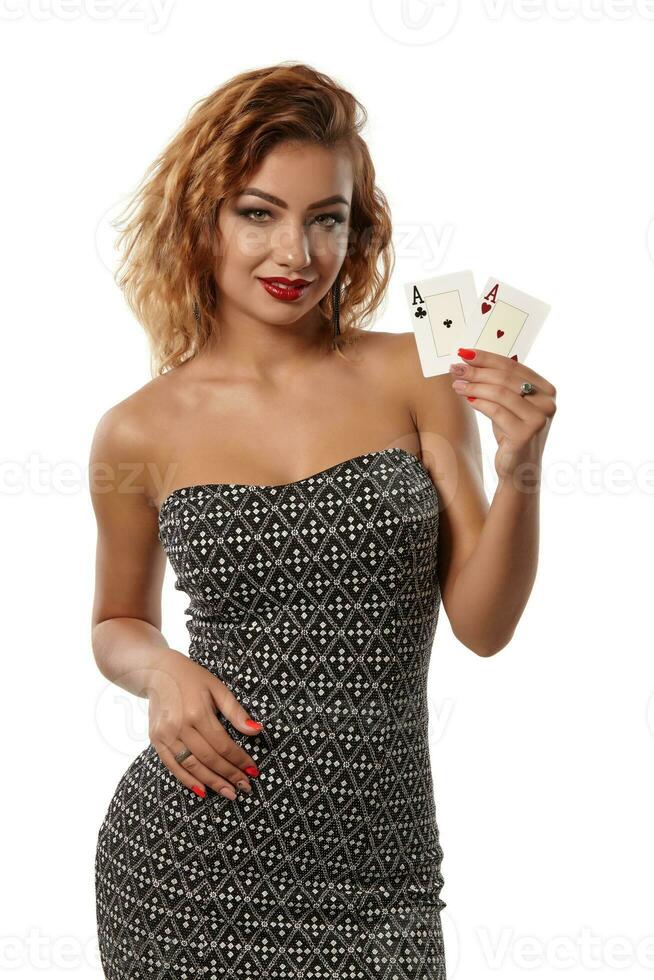 jengibre niña vistiendo gris vestir es posando participación dos jugando tarjetas en su manos en pie aislado en blanco antecedentes. casino, póker. de cerca disparo. foto