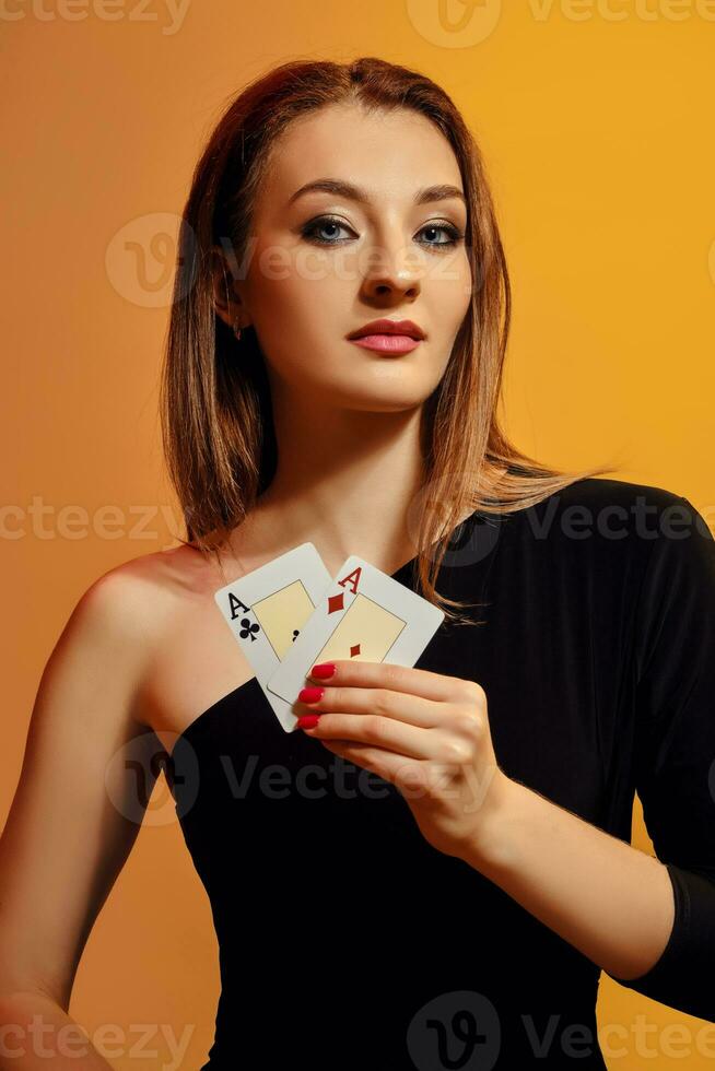 Blonde model with bright make-up, in black dress is showing two aces, posing against colorful background. Gambling, poker, casino. Close-up. photo