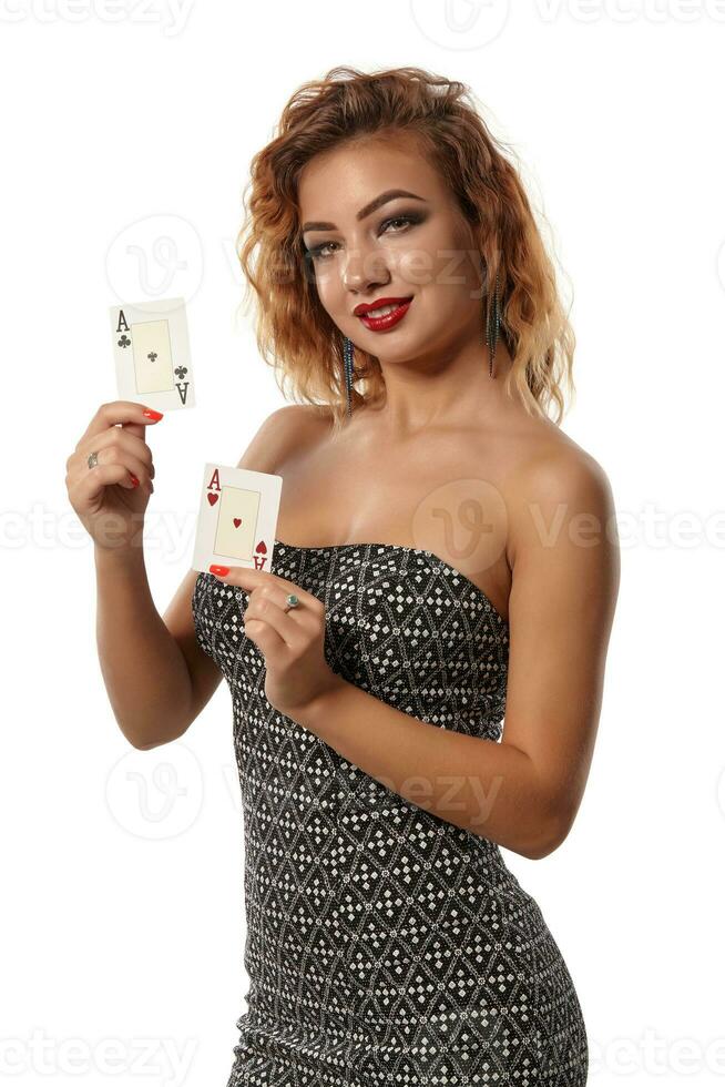 Ginger girl wearing gray dress is posing holding two playing cards in her hands standing isolated on white background. Casino, poker. Close-up shot. photo