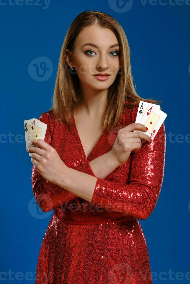 rubia mujer con constituir, en rojo lentejuela vestir es demostración cuatro ases, posando en azul antecedentes. juego, póker, casino. de cerca. foto