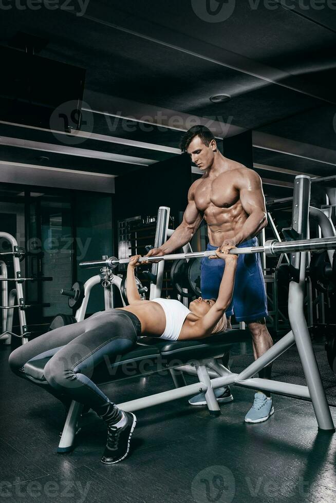 personal entrenador Ayudar un joven mujer levantar un barra con pesas mientras trabajando fuera en un gimnasio foto