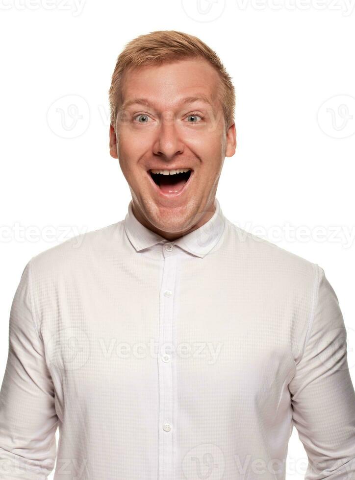 Imposing, young, blond man in a white shirt is grimacing while standing isolated on a white background photo