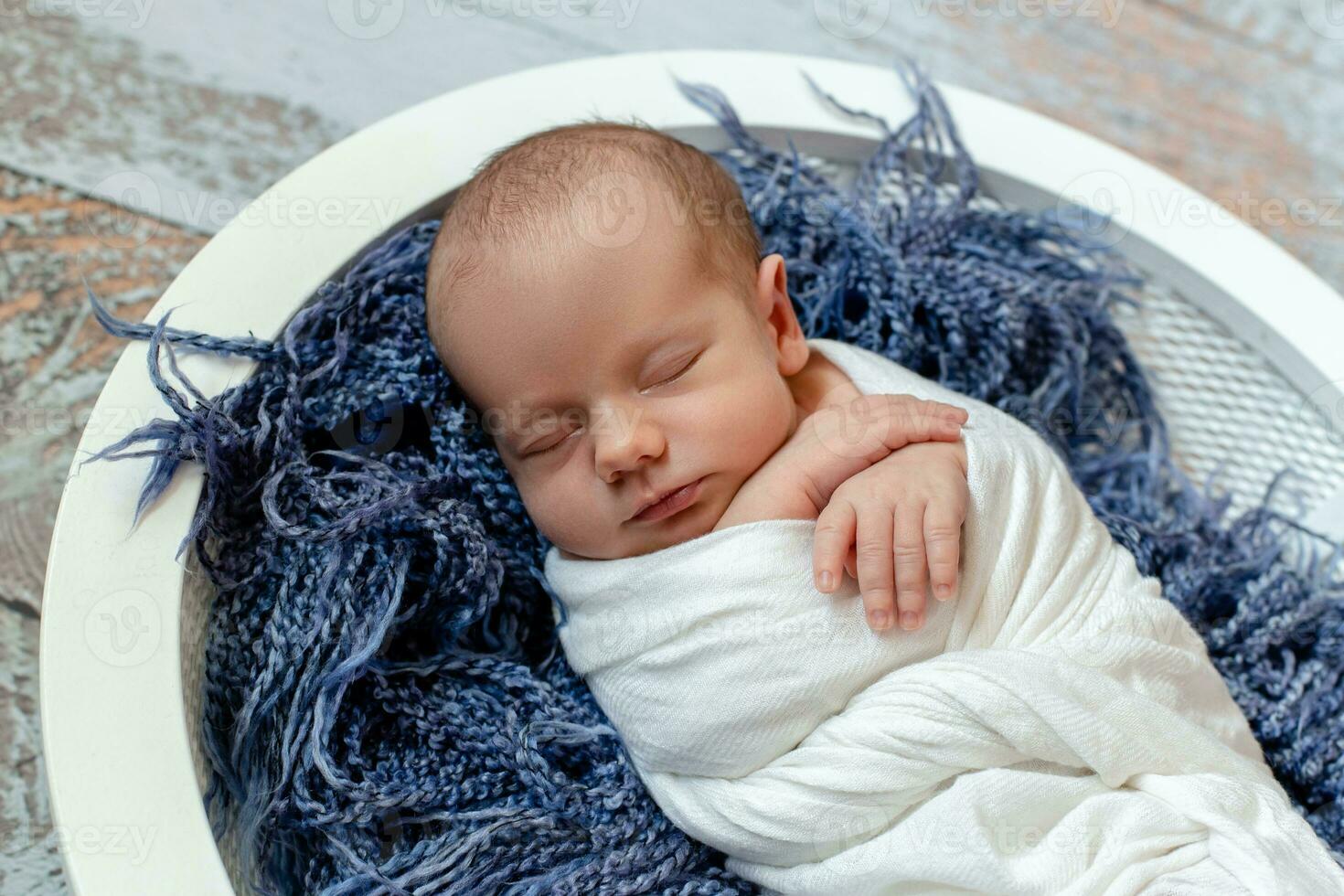 Little baby boy sleeping in a basket on the wooden floor, studio shot photo