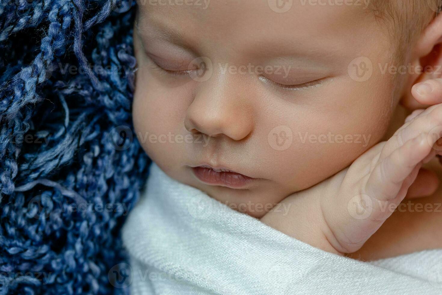 Newborn - baby, face close-up. The sleeping Newborn boy under a white knitted blanket lies on the blue fur. photo