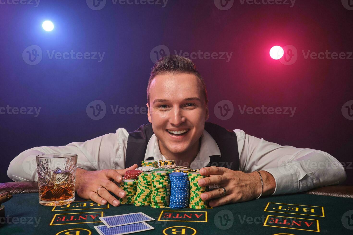 Wealthy man is posing at a poker table with chips and a glass of whiskey on it at a casino. photo