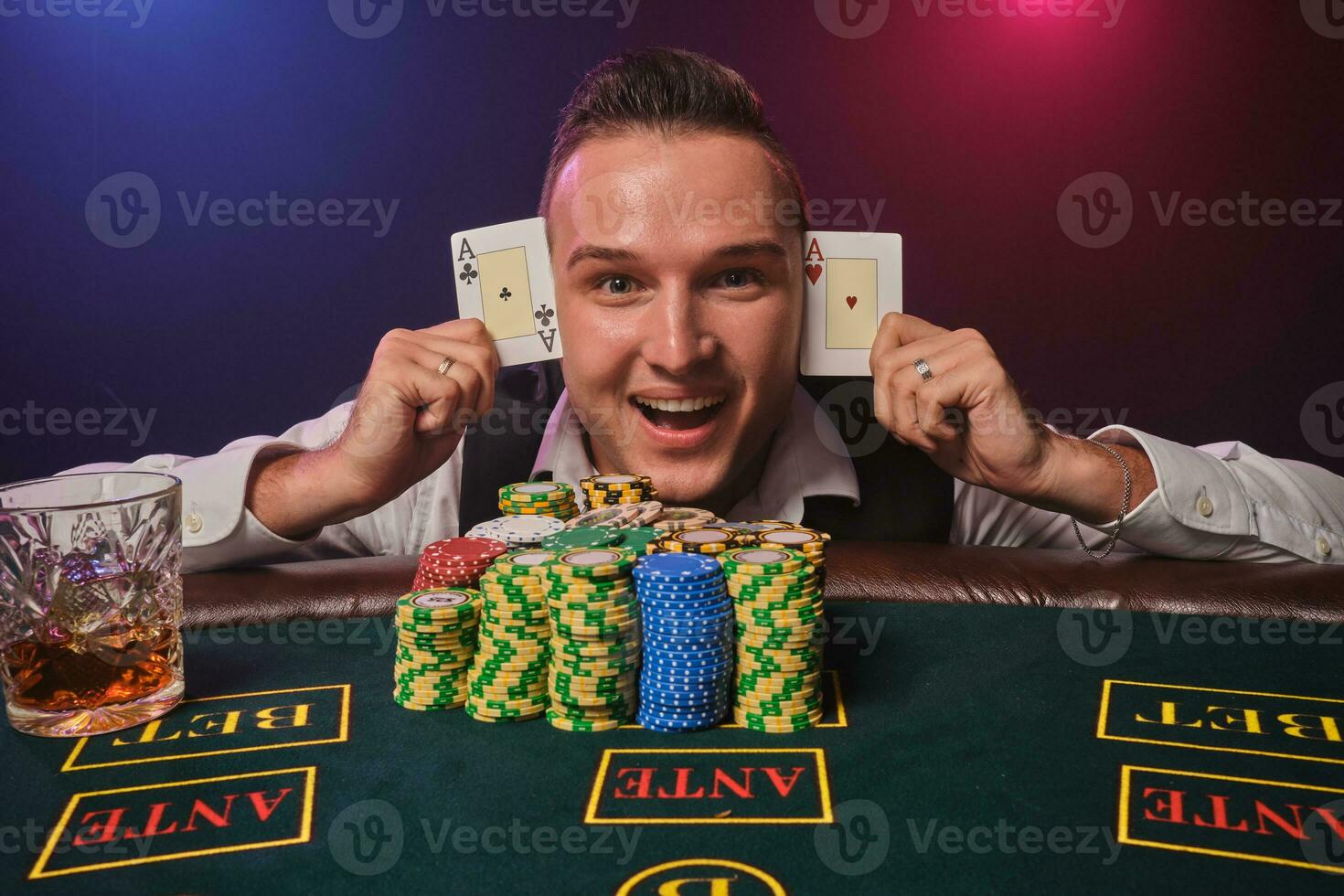 Wealthy man is posing at a poker table with chips and a glass of whiskey on it at a casino. photo