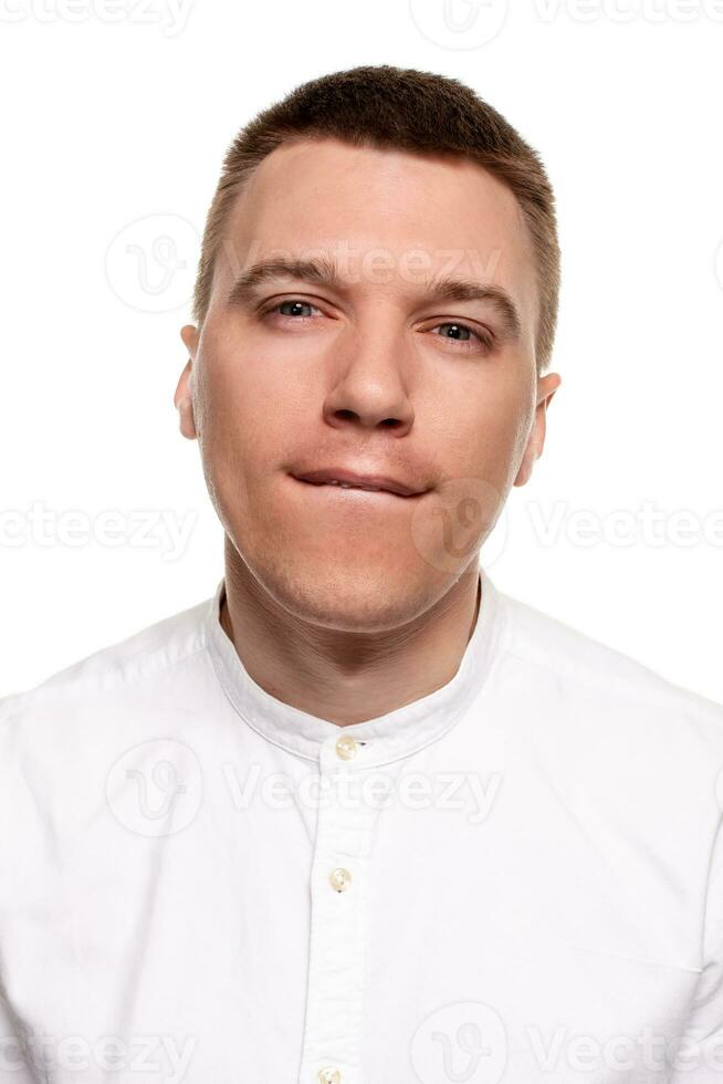 encantador hermoso joven hombre en un blanco camisa es haciendo caras, mientras en pie aislado en un blanco antecedentes foto