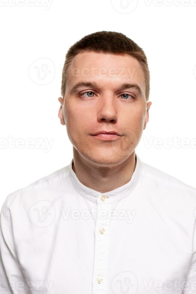 encantador hermoso joven hombre en un blanco camisa es haciendo caras, mientras en pie aislado en un blanco antecedentes foto