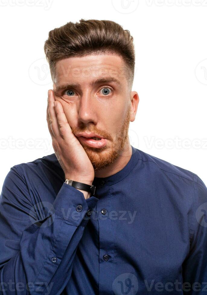 Studio portrait of gloomy european man showing boredom while leaning head on hand and standing over white background. photo