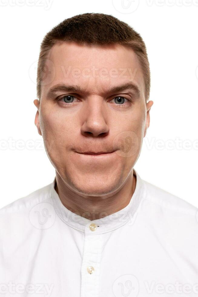 Charming handsome young man in a white shirt is making faces, while standing isolated on a white background photo