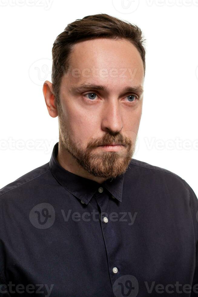 Portrait of a handsome, unshaven man, dressed in a dark blue shirt, standing against a white background. Self confident man. photo