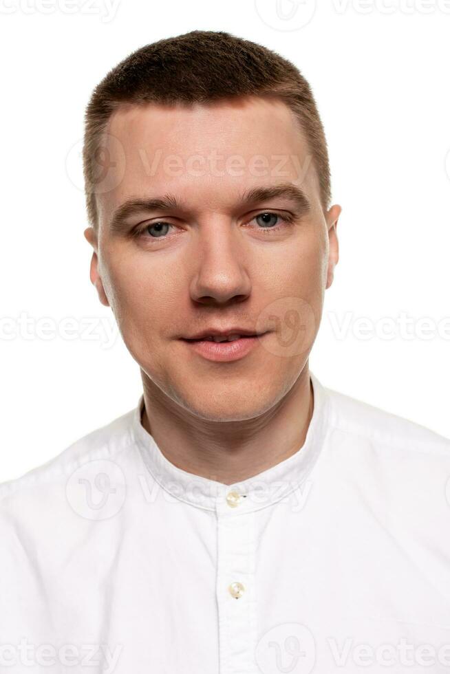 encantador hermoso joven hombre en un blanco camisa es haciendo caras, mientras en pie aislado en un blanco antecedentes foto