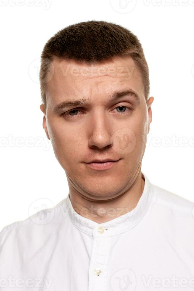 encantador hermoso joven hombre en un blanco camisa es haciendo caras, mientras en pie aislado en un blanco antecedentes foto