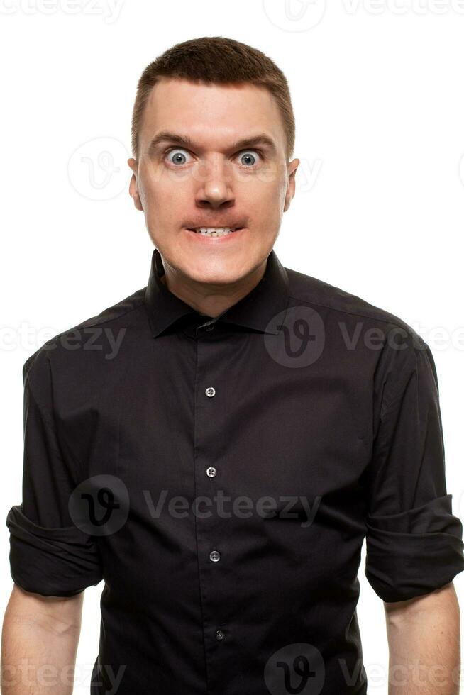 Handsome young man in a black shirt is making faces, while standing isolated on a white background photo