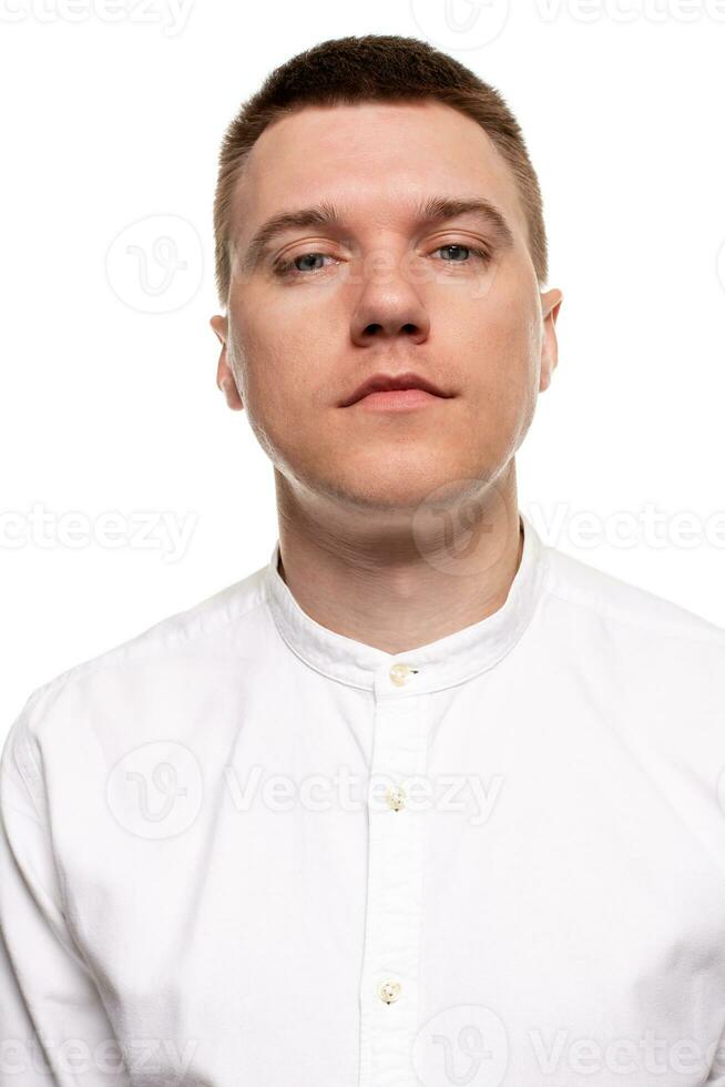 encantador hermoso joven hombre en un blanco camisa es haciendo caras, mientras en pie aislado en un blanco antecedentes foto