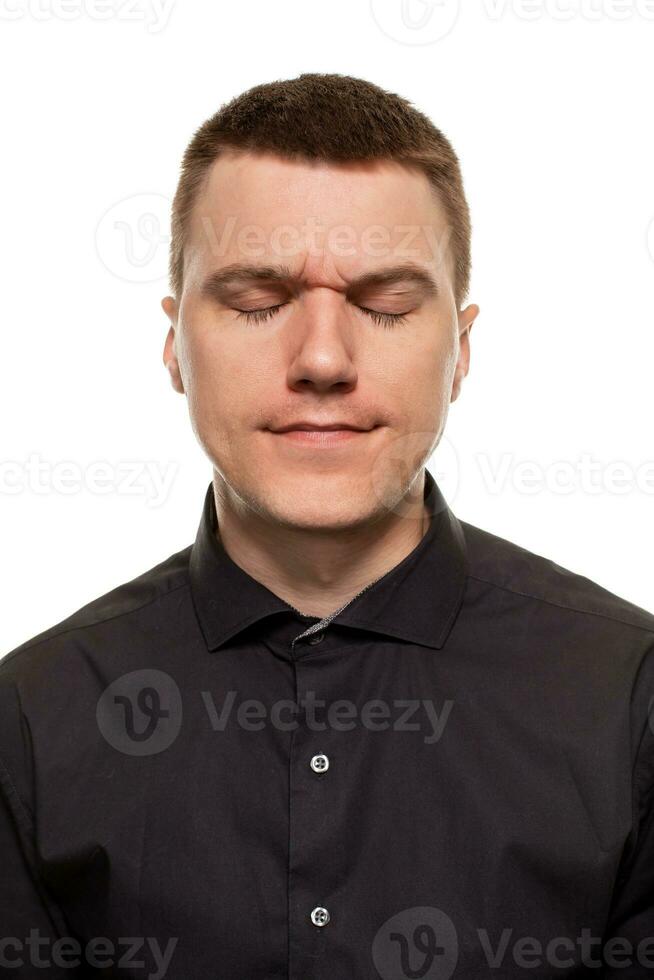 Handsome young man in a black shirt is making faces, while standing isolated on a white background photo