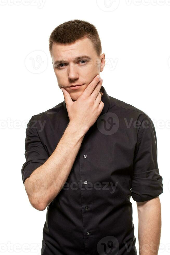 Handsome young man in a black shirt is making faces, while standing isolated on a white background photo