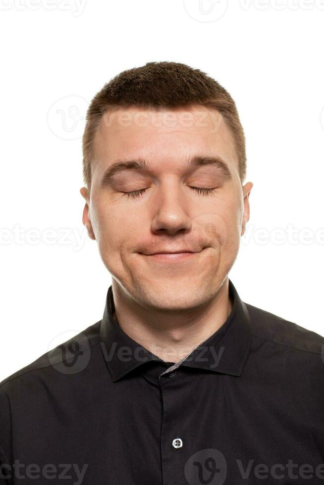 Handsome young man in a black shirt is making faces, while standing isolated on a white background photo