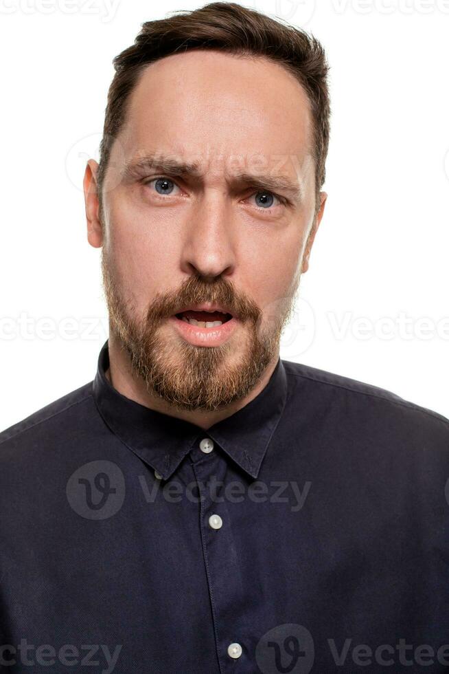 retrato de un elegante, sin afeitar hombre, vestido en un oscuro azul camisa, en pie en contra un blanco antecedentes. yo confidente hombre. foto