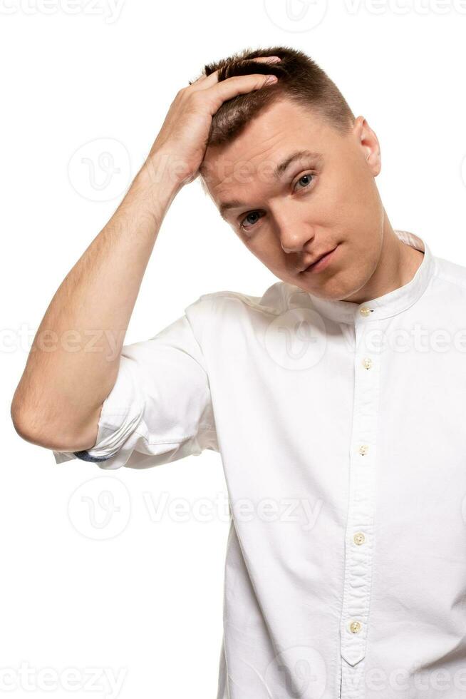 encantador hermoso joven hombre en un blanco camisa es haciendo caras, mientras en pie aislado en un blanco antecedentes foto