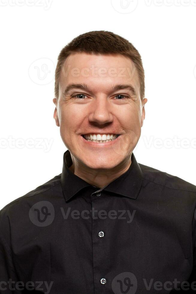 Handsome young man in a black shirt is making faces, while standing isolated on a white background photo