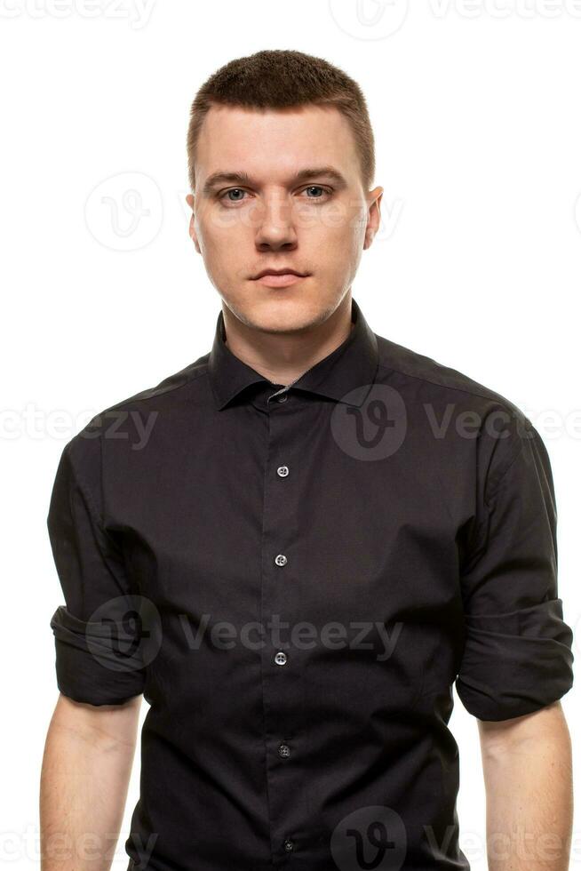 hermoso joven hombre en un negro camisa es haciendo caras, mientras en pie aislado en un blanco antecedentes foto